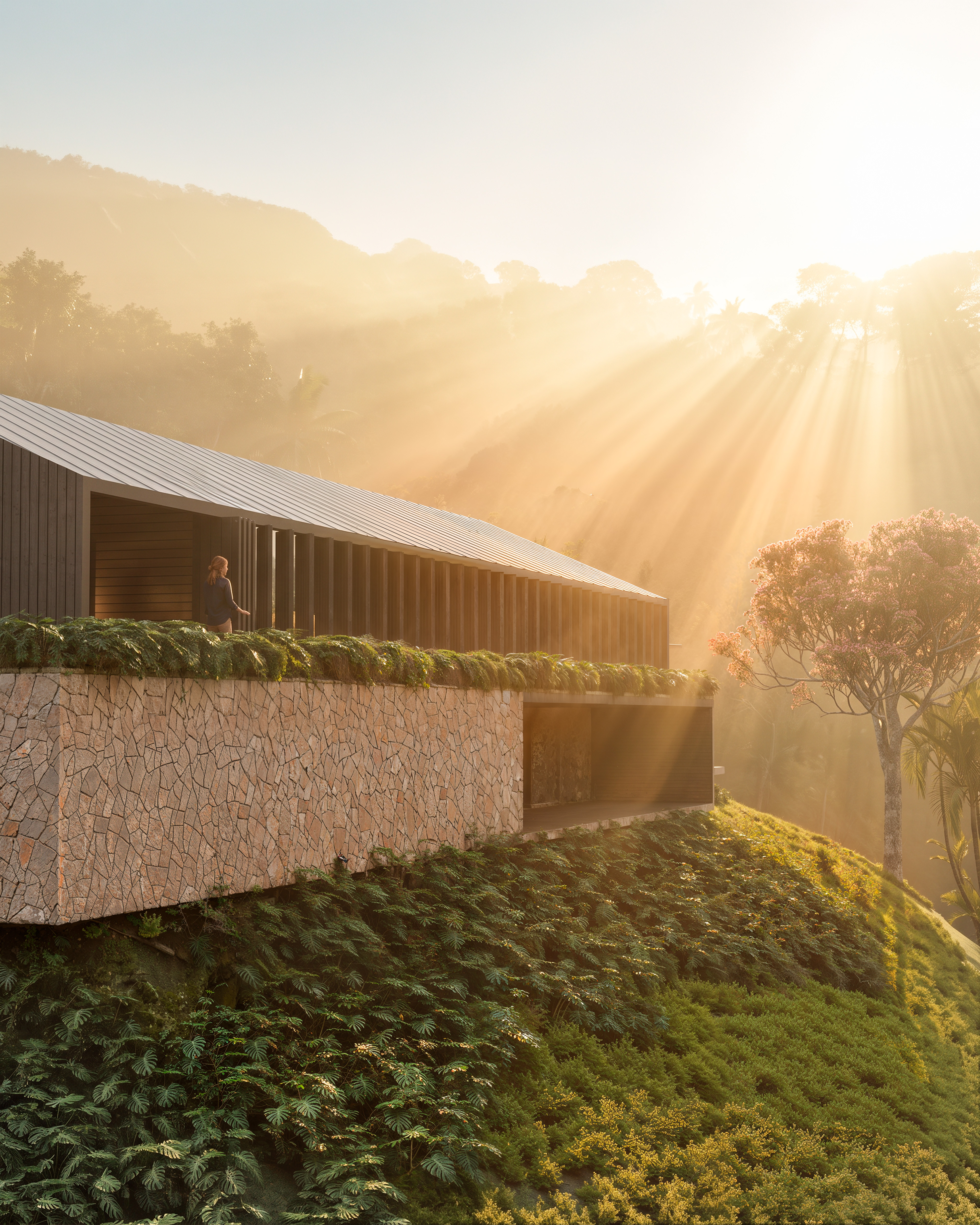 Fachada de pedra da Casa LG20 atravessada pela luz dourada do amanhecer na serra
